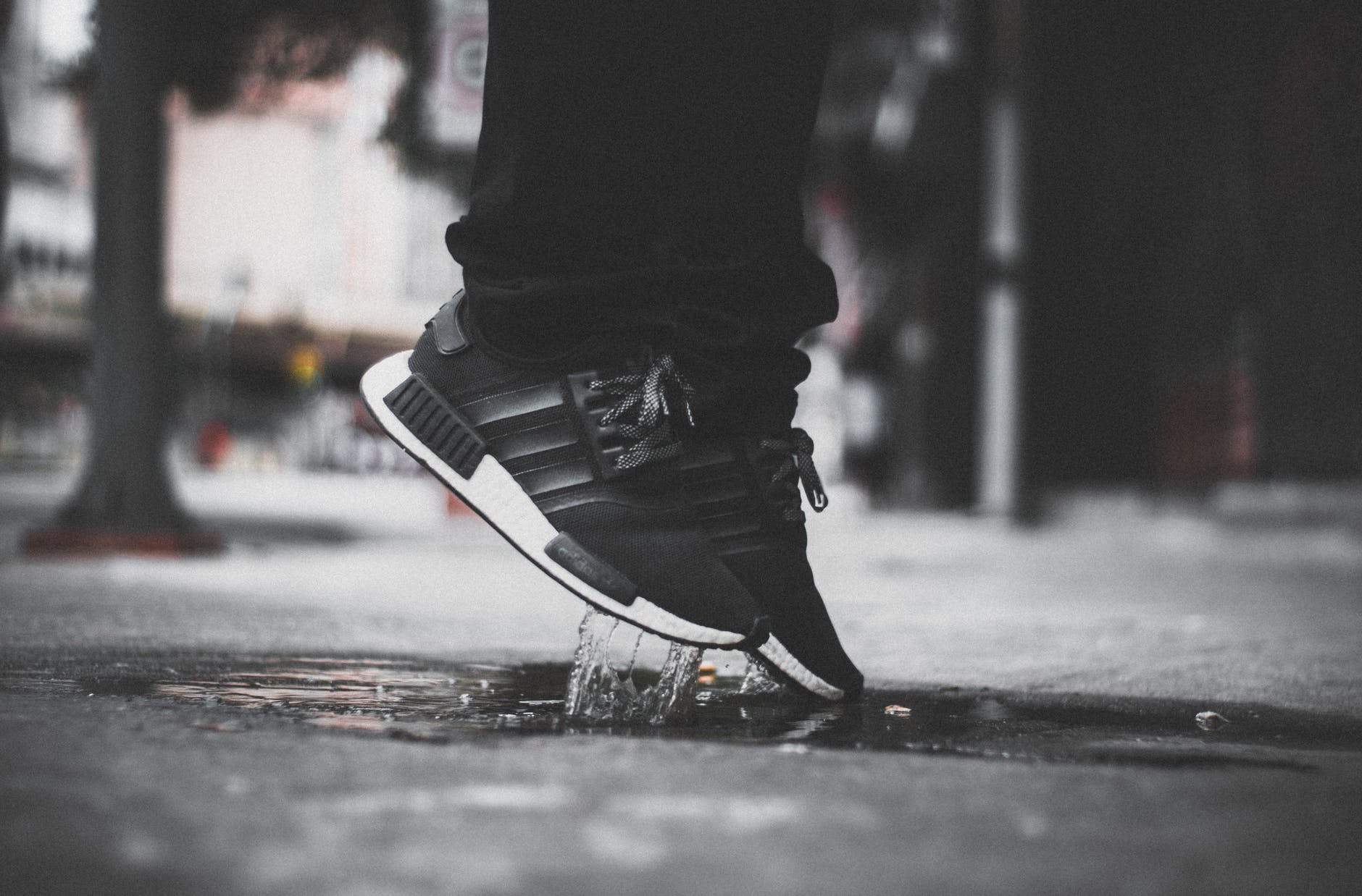 grayscale photo of person wearing adidas nmd jumping on puddle